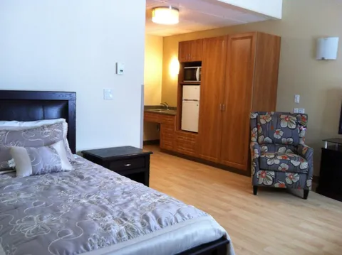Bedroom with a double bed, bedside table, floral armchair and kitchenette.