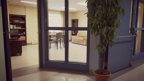 Glass doors beside a plant, with a sofa, table and bookshelf beyond