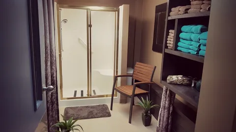 Bathroom with a glass shower enclosure, chair and shelves of towels
