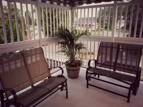 Benches and a potted plant on a covered porch with white railings
