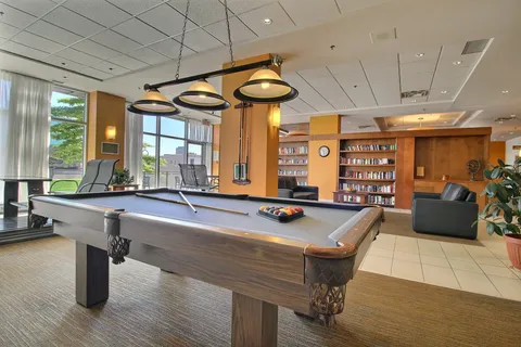 Billiards table beneath hanging lights beside seating and bookshelves