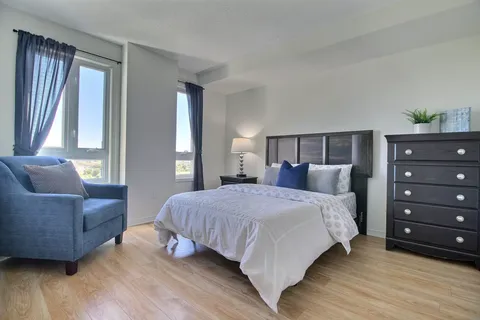Bedroom with a made bed, armchair and dark dresser