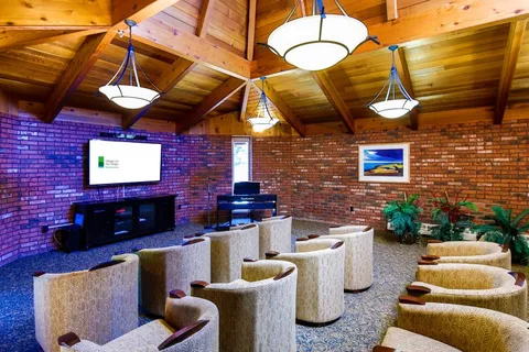 Room with rows of chairs facing a television beneath a wooden ceiling