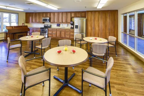 Room with round tables, chairs, a piano and a kitchen area