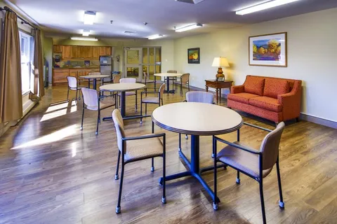 Room with round tables, chairs, an orange sofa and a kitchen area