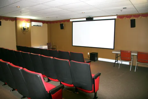 Cinema room with rows of black and red seats facing a blank projection screen