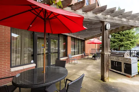 Patio seating beneath umbrellas beside a pergola and barbecue