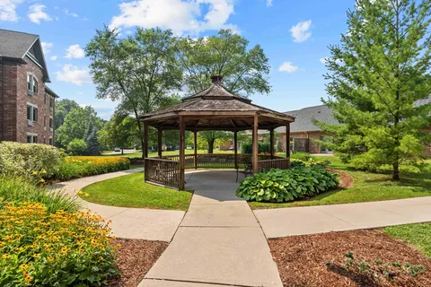 Wooden gazebo among flower beds, trees and paved paths
