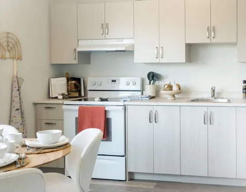 Suite kitchen with white cupboards, a stove and a dining table.