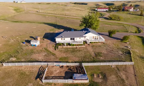 Aerial view of a single-storey house with a fenced yard and surrounding fields