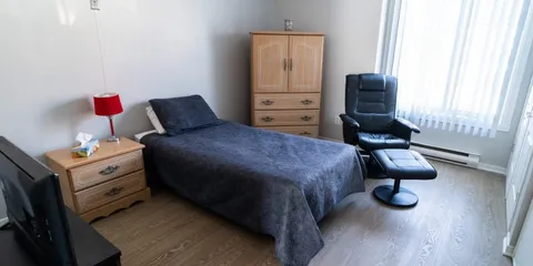 Bedroom with a grey bedspread, wooden cabinet and a black armchair