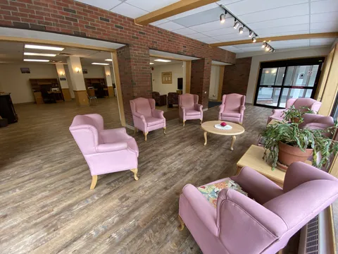 Open lounge with pink upholstered chairs, round tables, brick columns and plants.