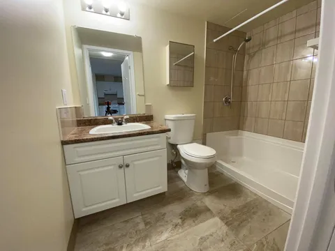 Bathroom with a white vanity, mirror, toilet and tiled bathtub.