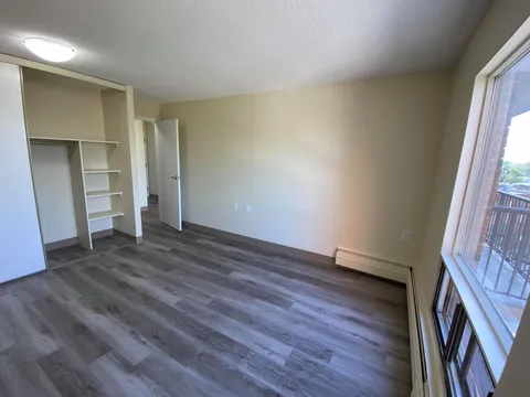 Empty bedroom with an open closet, shelving and a balcony door.