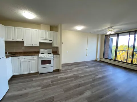 Empty suite with a white kitchenette, wood-look flooring and a balcony door.