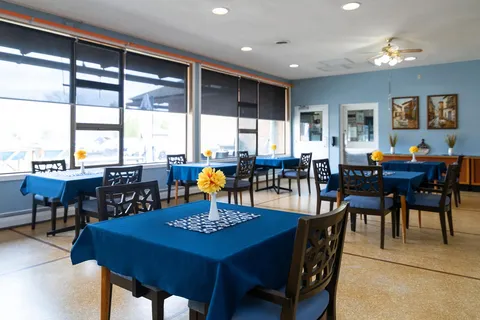 Dining tables with blue cloths and dark wooden chairs beside windows
