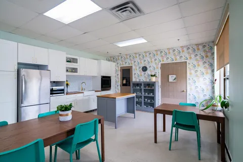 Room with tables, green chairs and kitchen cabinets