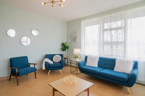 Room with a blue sofa, two armchairs and round wall mirrors