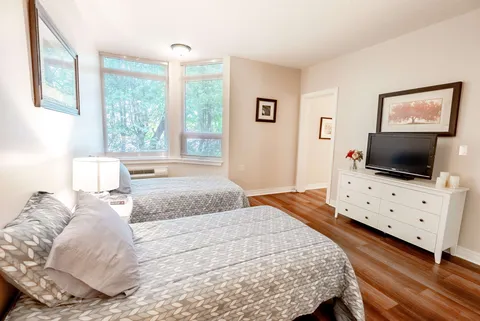 Bedroom with two beds, a dresser, television and corner windows