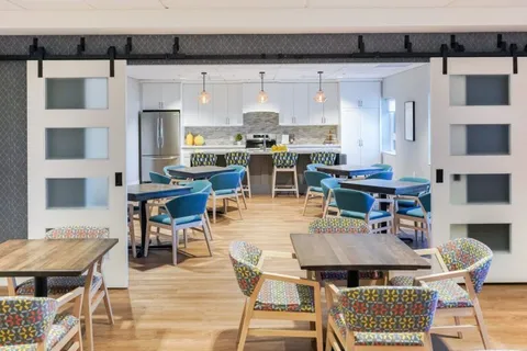 Room with dining tables and blue chairs beside a kitchen counter