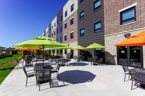 Multistorey brick building beside a patio with tables, chairs and colourful umbrellas