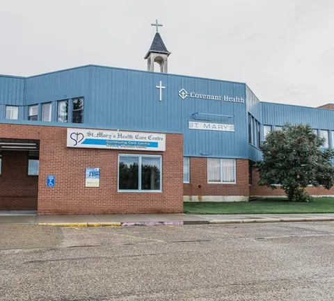 Low-rise brick building with blue siding, a bell tower and a tree beside the entrance