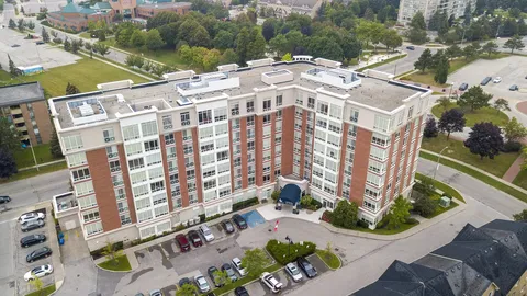 Aerial view of a brick and white multi-storey building with a covered entrance and parking