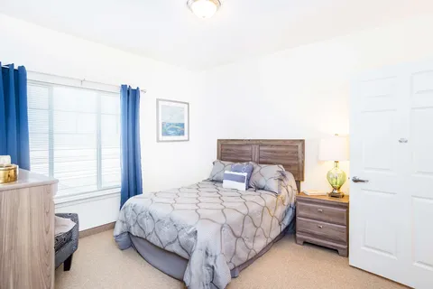 Bedroom with a bed, bedside table, lamp, dresser and blue curtains