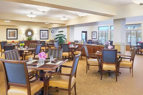 Dining room with tables, wooden chairs, flowers, framed pictures and large windows