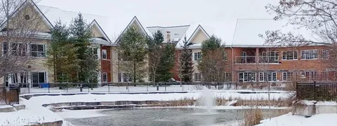 Building with steep roofs, balconies and trees beyond a pond with a fountain and snow