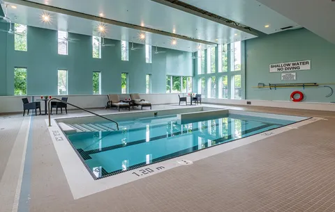Indoor swimming pool beside tall windows and lounge chairs