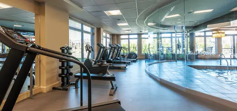 Fitness room with exercise equipment beside windows overlooking an indoor pool