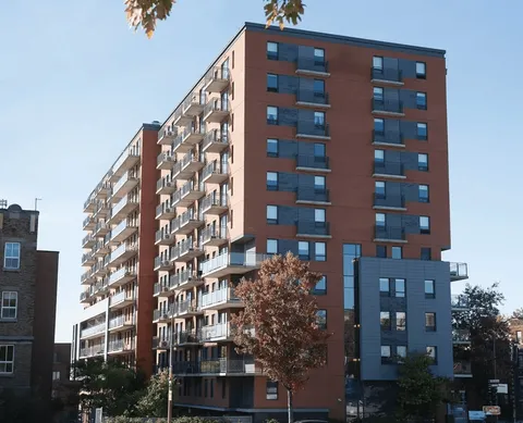 Tall brick residence with balconies beside trees and nearby buildings