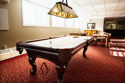 Pool table beneath a stained-glass light beside wooden tables and chairs