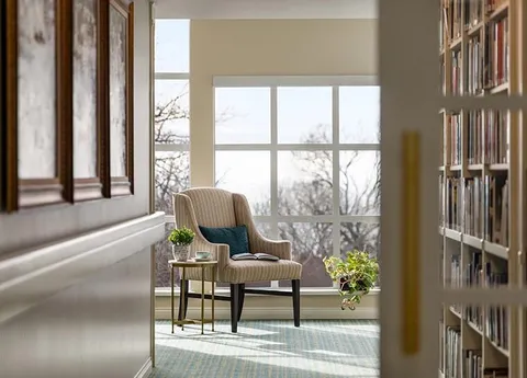 Library shelves and an armchair beside waterfront-facing windows.