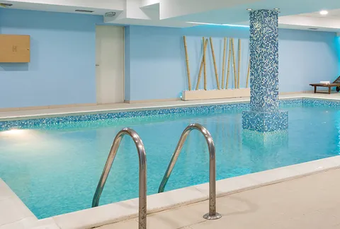 Indoor swimming pool with tiled columns and metal entry rails.
