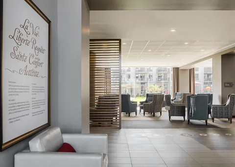 Armchairs beside large windows, with a sofa and framed sign in the foreground