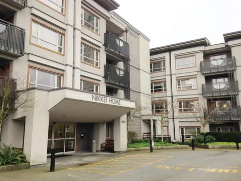 Four-storey building with balconies, a covered entrance and planted beds.