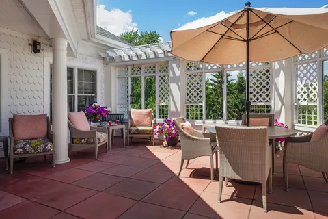 Patio with wicker chairs, tables, umbrellas and flowering planters.