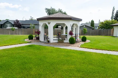 White garden gazebo beside paved paths and flower planters.