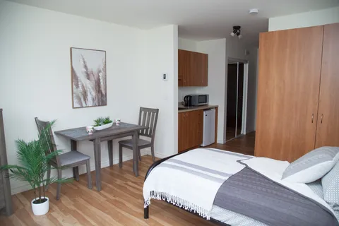 Suite with a bed, a small table and chairs, wooden cupboards and a kitchenette