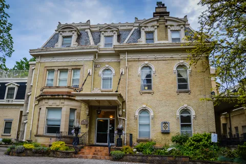 Brick building with a porch, front garden and tall trees