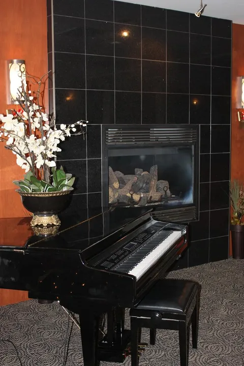 Black piano beside a tiled fireplace and a vase of flowers