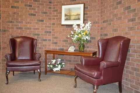 Two brown leather armchairs beside a wooden table and brick wall