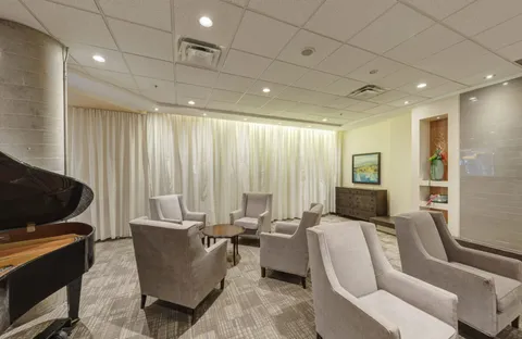 Armchairs and small tables beside a grand piano and curtained windows