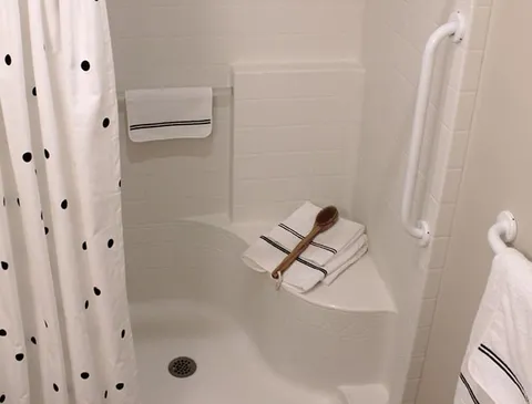 White shower with grab bars, a seat, towels and a patterned curtain
