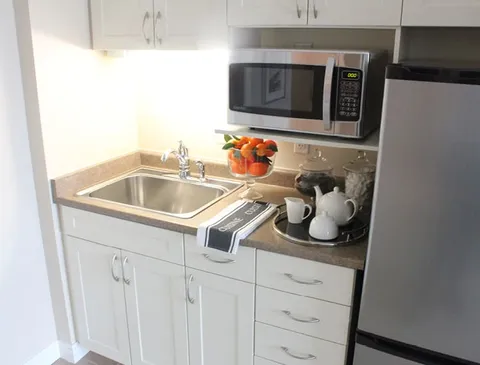Kitchenette with a sink, microwave, refrigerator and white cabinets