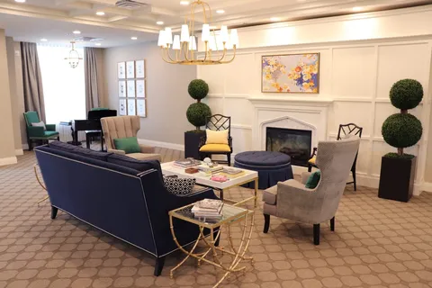 Lounge with a fireplace, navy sofa, armchairs, coffee tables and a grand piano