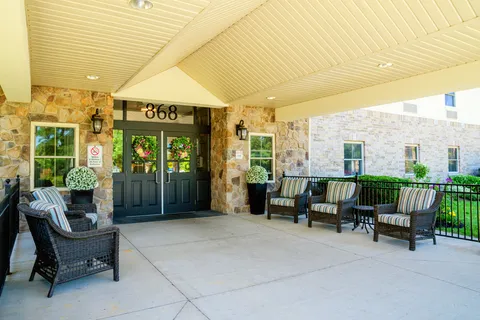 Covered entrance with double doors, stone walls and cushioned patio chairs