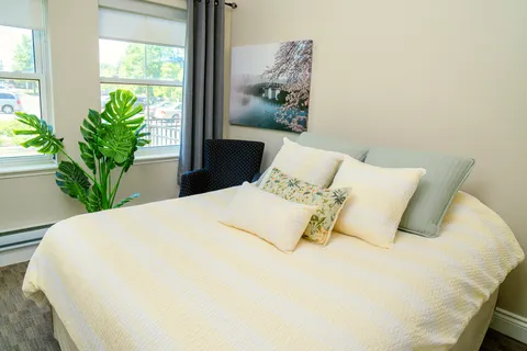 Bedroom with a bed, yellow cushions, a window and framed landscape artwork